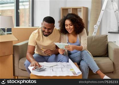mortgage, moving and real estate concept - happy african american couple with blueprint and calculator counting money for repair costs to new home. couple with blueprint counting money at home