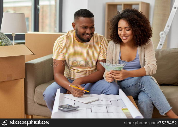 mortgage, moving and real estate concept - happy african american couple with blueprint and calculator counting money for repair costs to new home. couple with blueprint counting money at home