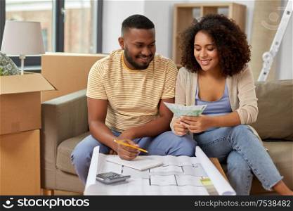 mortgage, moving and real estate concept - happy african american couple with blueprint and calculator counting money for repair costs to new home. couple with blueprint counting money at home