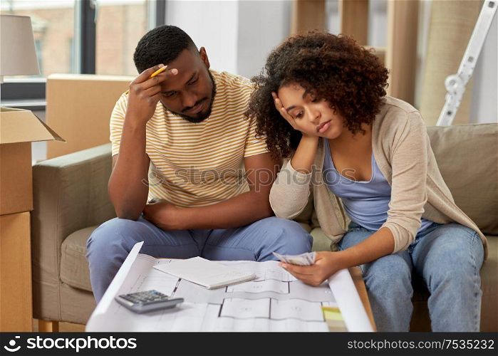 mortgage, moving and real estate concept - sad african american couple with blueprint and calculator counting money for repair costs to new home. sad couple with blueprint counting money at home