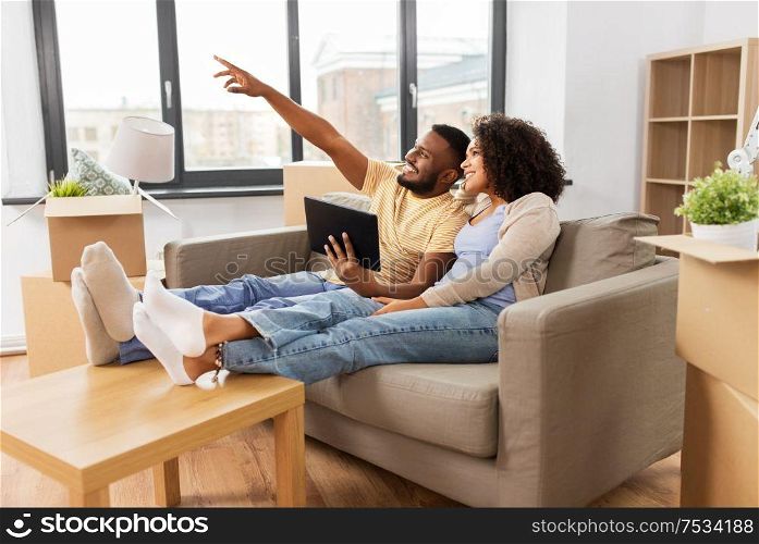 mortgage, people and real estate concept - happy african american couple with tablet pc computer sitting on sofa at new home. happy couple with tablet pc computer at new home