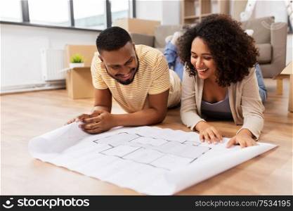 mortgage, people and real estate concept - happy african american couple with boxes and blueprint moving to new home. couple with boxes and blueprint moving to new home