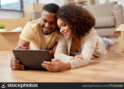 mortgage, people and real estate concept - happy african american couple with tablet pc computer lying on floor at new home. happy couple with tablet pc computer at new home