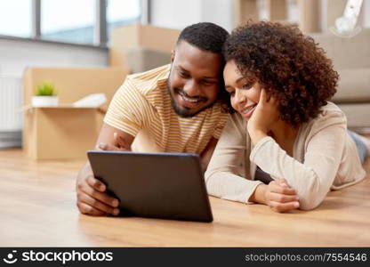 mortgage, people and real estate concept - happy african american couple with tablet pc computer lying on floor at new home. happy couple with tablet pc computer at new home