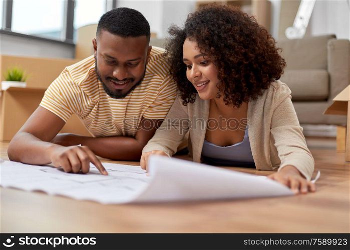 mortgage, people and real estate concept - happy african american couple with boxes and blueprint moving to new home. couple with boxes and blueprint moving to new home