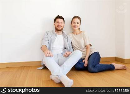 mortgage, people and real estate concept - happy couple sitting on floor at empty room of new home. happy couple at empty room of new home