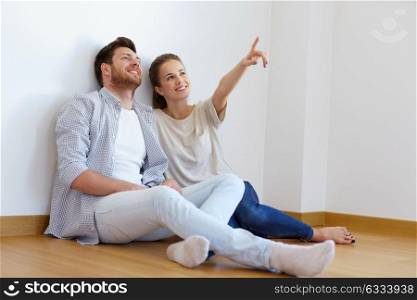 mortgage, people and real estate concept - happy couple sitting on floor at empty room of new home. happy couple at empty room of new home
