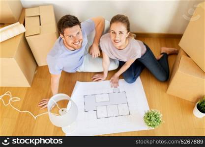 mortgage, people and real estate concept - happy couple with boxes and blueprint moving to new home. couple with boxes and blueprint moving to new home