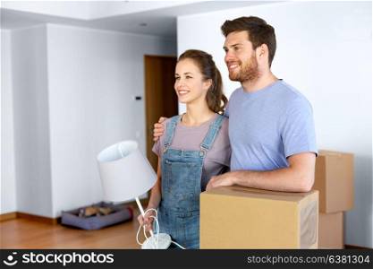 mortgage, people and real estate concept - happy couple with boxes and lamp moving to new home. couple with boxes and lamp moving to new home