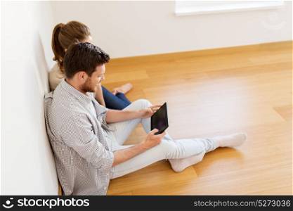 mortgage, people and real estate concept - happy couple with tablet pc computer at empty room of new home. happy couple with tablet pc computer at new home