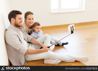 mortgage, people, housing and real estate concept - happy family with child taking picture by smartphone selfie stick at new home. family taking selfie by smartphone at new home