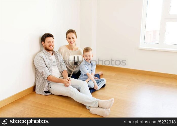 mortgage, people, housing and real estate concept - happy family with child taking picture by smartphone selfie stick at new home. family taking selfie by smartphone at new home