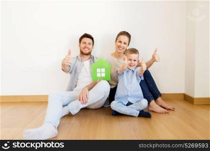 mortgage, people, housing and real estate concept - happy family with green paper house moving to new home and showing thumbs up. family with green house showing thumbs up at home