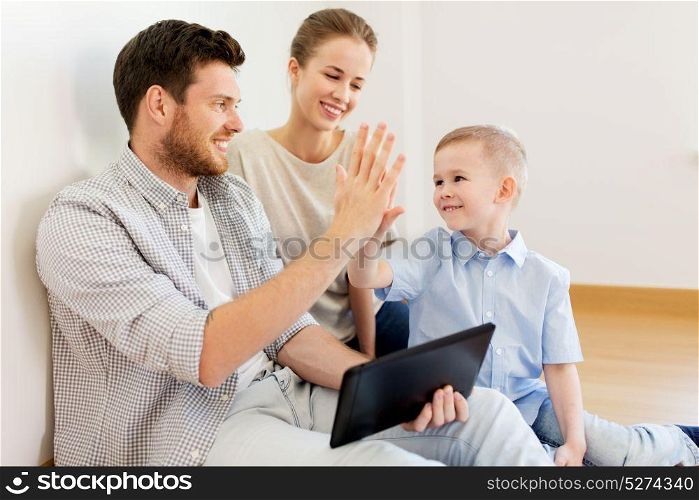 mortgage, people, housing and real estate concept - happy family with tablet pc computer at new home making high five gesture. family with tablet pc at new home making high five