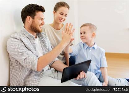 mortgage, people, housing and real estate concept - happy family with tablet pc computer at new home making high five gesture. family with tablet pc at new home making high five