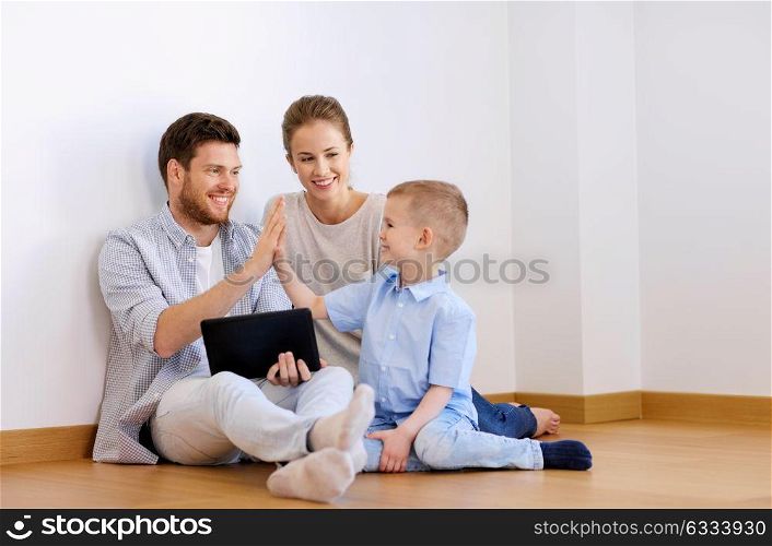 mortgage, people, technology and real estate concept - happy family with tablet pc computer at new home making high five gesture. family with tablet pc at new home making high five
