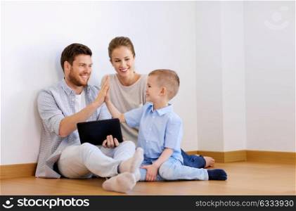 mortgage, people, technology and real estate concept - happy family with tablet pc computer at new home making high five gesture. family with tablet pc at new home making high five