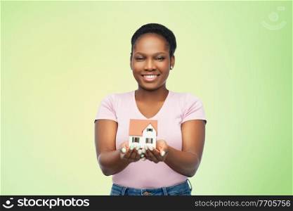 mortgage, real estate and accommodation concept - happy smiling african american woman holding house model over green background. smiling african american woman holding house model