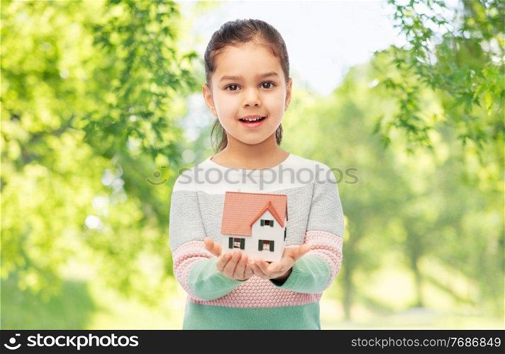 mortgage, real estate and accommodation concept - smiling girl holding house model over green natural background. smiling girl holding house model
