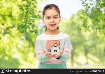 mortgage, real estate and accommodation concept - smiling girl holding house model over green natural background. smiling girl holding house model