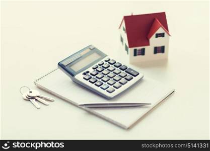 mortgage, real estate and property concept - close up of home model, house keys, calculator and notebook with pen. close up of home model, calculator and notebook