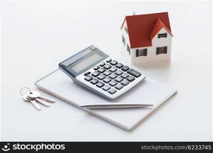 mortgage, real estate and property concept - close up of home model, house keys, calculator and notebook with pen