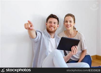 mortgage, technology and real estate concept - happy couple with tablet pc computer at empty room of new home. happy couple with tablet pc computer at new home