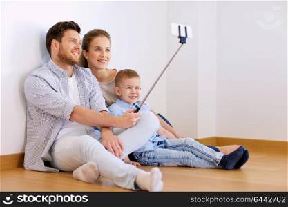 mortgage, technology and real estate concept - happy family with child taking picture by smartphone selfie stick at new home. family taking selfie by smartphone at new home