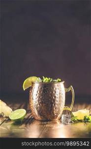 Moscow mule alcoholic cocktail in copper mug with crushed ice, mint and lemon over minton dark wooden table with amazing backlight, copy space. Close up view, copy space