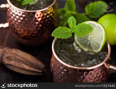 Moscow mule cocktail in a copper mug with lime and mint and wooden squeezer on dark wooden table background. Macro