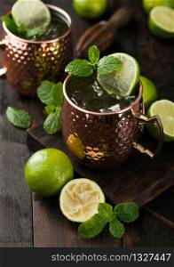 Moscow mule cocktail in a copper mug with lime and mint and wooden squeezer on dark wooden table background.