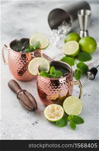 Moscow mule cocktail in a copper mug with lime and mint and wooden squeezer on light kitchen table background with steel shaker and jigger