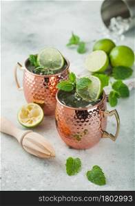 Moscow mule cocktail in a copper mug with lime and mint and wooden squeezer on light kitchen table background with steel shaker