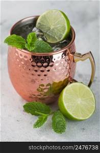 Moscow mule cocktail in a copper mug with lime and mint on light kitchen table background
