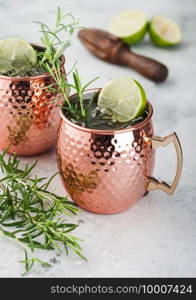 Moscow mule cocktail in a copper mug with lime and rosemary and wooden squeezer on light kitchen table background