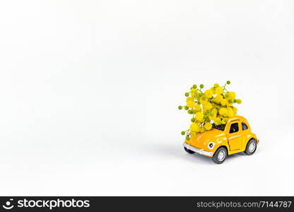 Moscow, Russia - February 23, 2019: 8 March International Women&rsquo;s Day card with toy model retro car delivering bouquet of mimosa flowers on white background. Valentine&rsquo;s day, Flower delivery concept