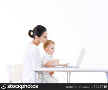 Mother and 2 years old baby boy sitting at the desk and using laptop computer.