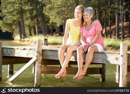 Mother and adult daughter sitting by lake