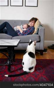 Mother and baby boy lying on sofa looking at cat