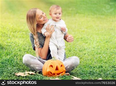 Mother and baby enjoying Halloween holiday outdoor, sitting on fresh green grass field, traditional festive decoration, family fun
