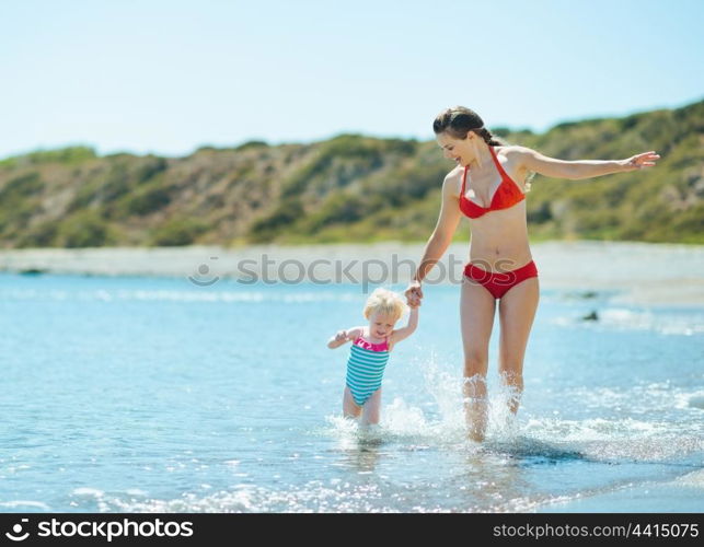 Mother and baby girl running on sea coast