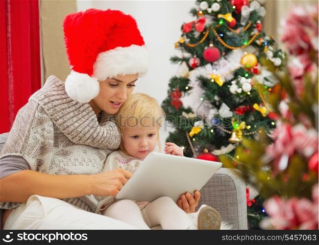 Mother and baby girl using tablet PC near Christmas tree