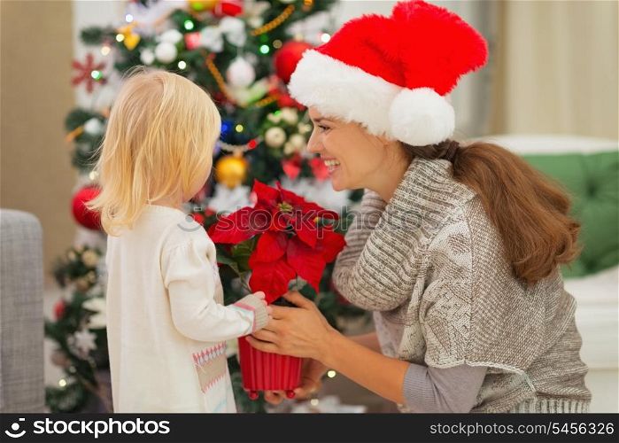 Mother and baby girl with Christmas rose near Christmas tree