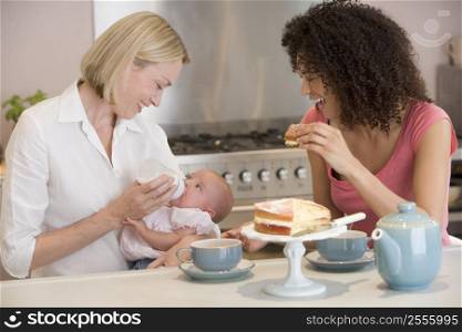 Mother and baby in kitchen with friend eating cake and smiling