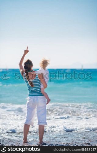 Mother and baby on sea coast pointing on copy space