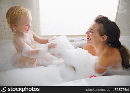 Mother and baby playing with foam in bathtub