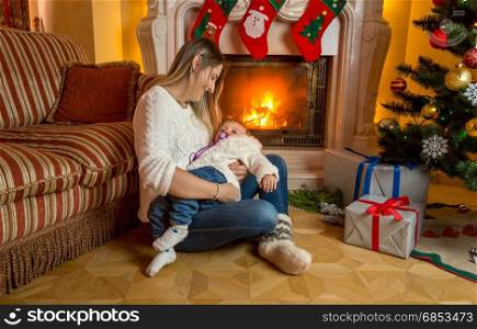 Mother and baby sitting on floor at fireplace decorated for Christmas