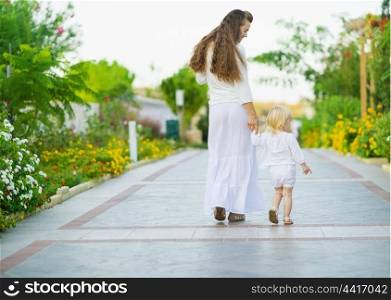 Mother and baby walking outdoors. Rear view