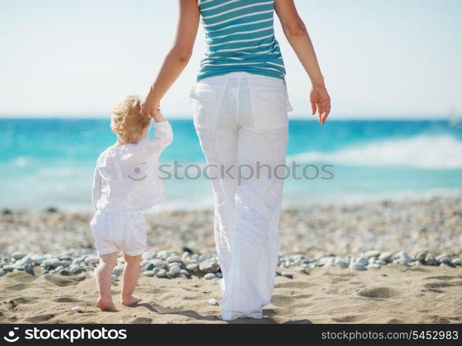 Mother and baby walking to sea. Rear view