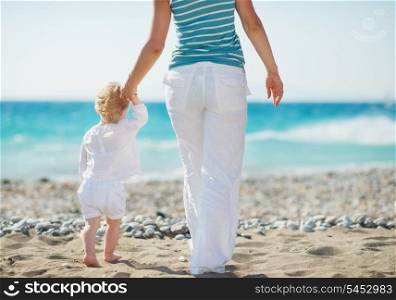 Mother and baby walking to sea. Rear view